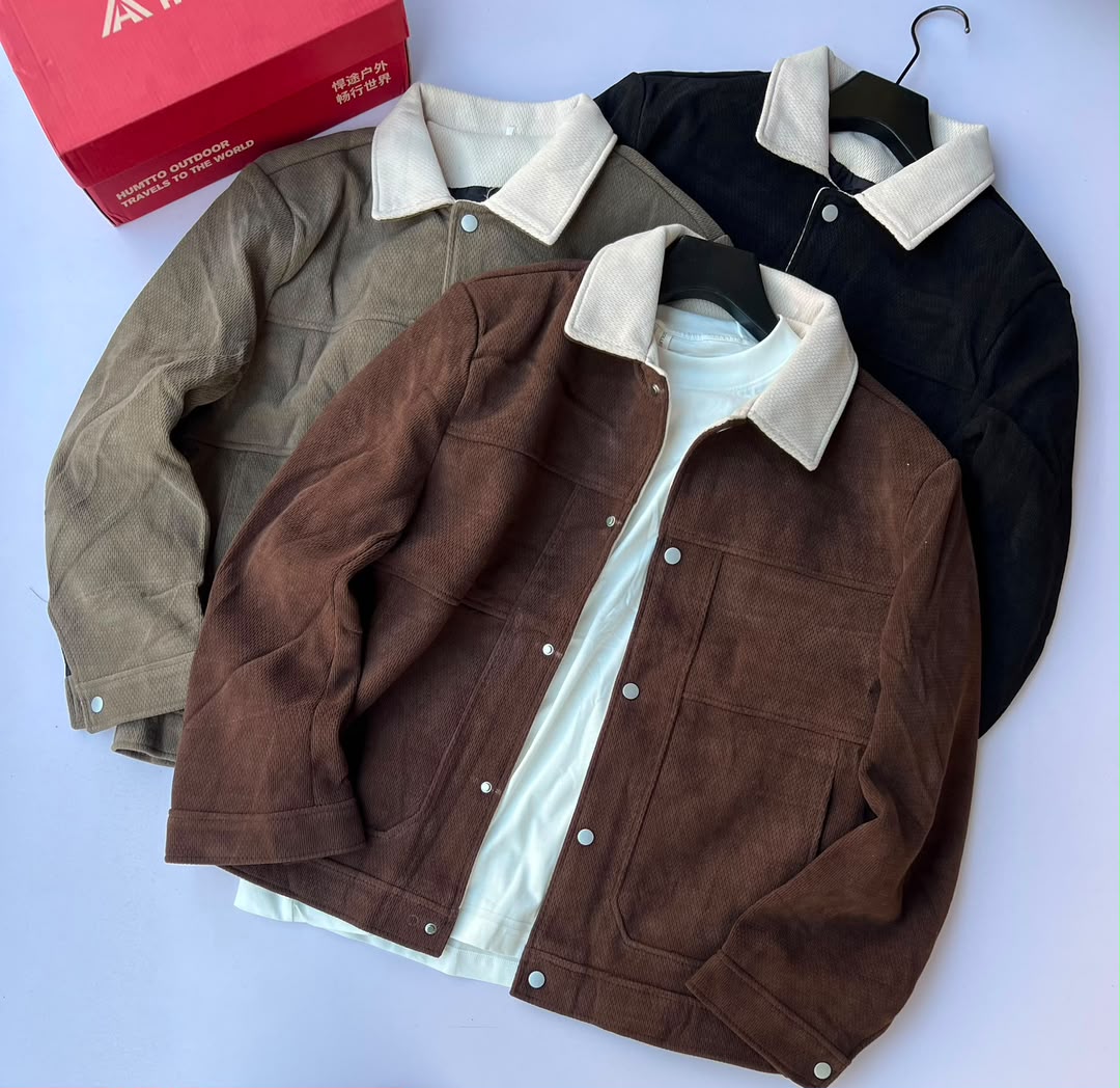 A classic button-snap, casual workwear-style jacket made from textured corduroy fabric. It features a contrasting cream sherpa/felt turn-down collar, front snap-button closure, dual chest stitch detailing with side entry hand pockets, and a buttoned hem. Shown in brown, olive tan, and black colorways.