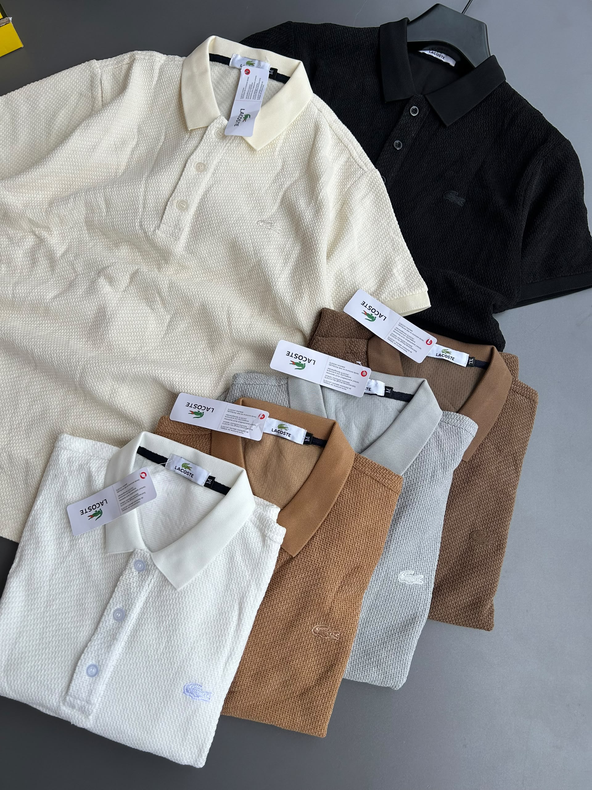 Lacoste Men's Textured Short-Sleeve Polo Shirt features a fine-knit textured weave with a classic three-button placket, neat collar, and signature embroidered crocodile logo on the chest, shown in tan and white.