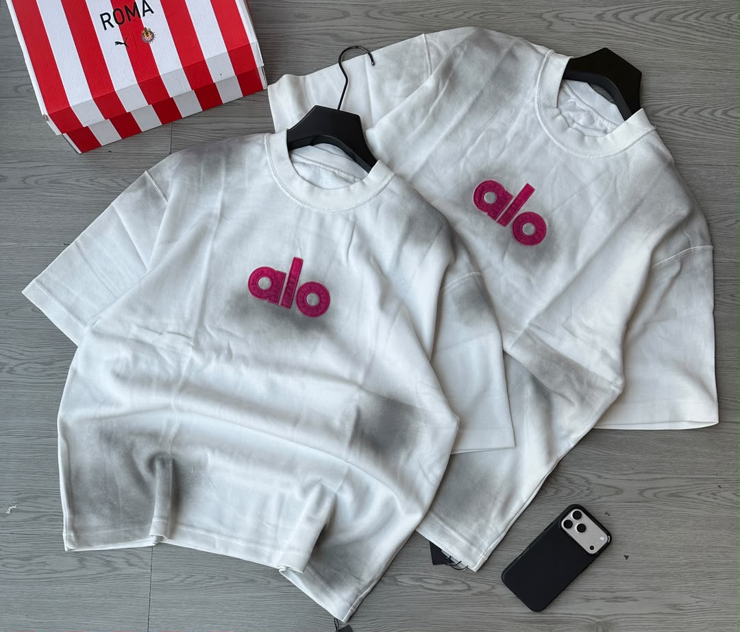 crew-neck t-shirt made from heavy cotton, featuring a bold, bright pink "alo" chest logo print in a casual, relaxed fit.